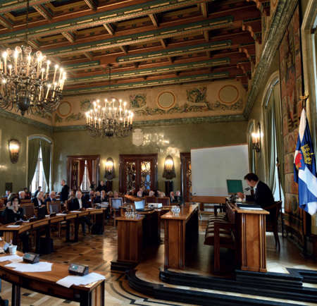 (154) Chorągiew miasta każdorazowo towarzyszy obradom Rady Miasta Krakowa na jej sesjach zarówno uroczystych, jak i zwyczajnych oraz nadzwyczajnych
– na czas obrad usytuowana zostaje u szczytu podium prezydialnego, z jego lewej strony; po prawej stronie podium znajduje się laska przewodniczącego.
Na zdjęciu posiedzenie zwyczajne 9 października 2019 r. (z zasobów UMK)