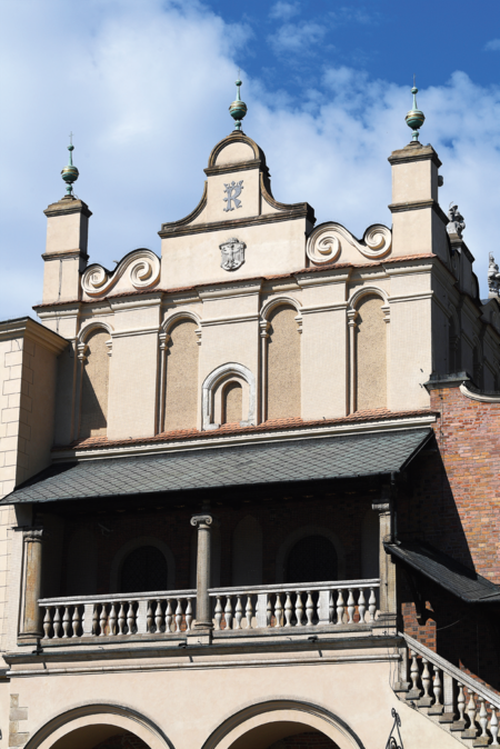 (268) Ukoronowany królewski monogram „K” na południowej stronie Sukiennic, od wylotu ul. Brackiej – po przebudowie w latach 1875–1879 prowadzonej
według projektu Tomasza Prylińskiego; widoczny monogram kazimierzowski prawdopodobnie umieszczono ówcześnie dla upamiętnienia Kazimierza
Wielkiego mającego zasadniczy udział w powstaniu Sukiennic; znak ten teraz jednak odczytywany jest jako symbol miasta Krakowa (z zasobów UMK)